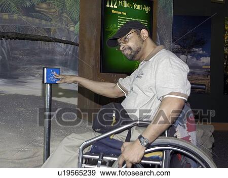 Stock Photo - Man with a disability, using a wheelchair accessible entrance while visiting an exhibit.. Fotosearch
