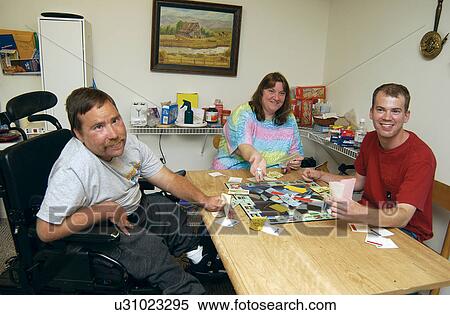 Stock Photography - Three friends playing a board game and having a good time. The two men have disabilities, and live in the apartment together.. Fotosearch
