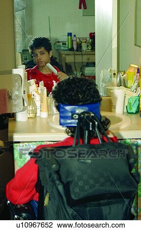 Stock Image - Woman with a disability checking her look as she is in the process of brushing her hair.. Fotosearch