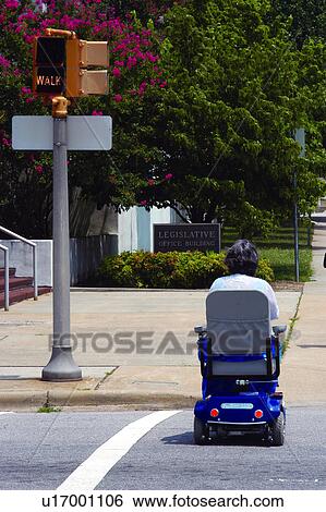 Stock Photograph - Woman with a disability using a motorized scooter for mobility crossing the street at a cross walk.. Fotosearch