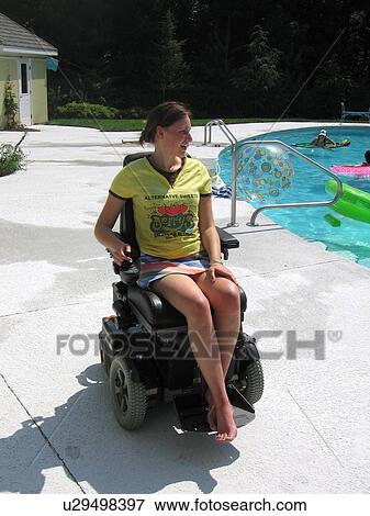 Stock Photo - Young woman (electric wheelchair user) watches family members in their accessible pool.. Fotosearch