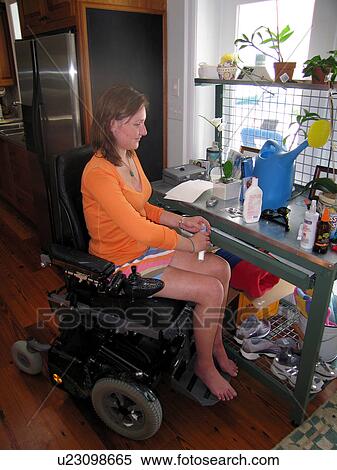 Stock Photography - Young woman (electric wheelchair user) works at a potting table.. Fotosearch