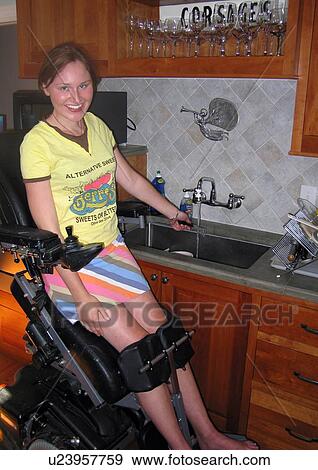 Stock Photo - Young woman elevates her power wheelchair to clean dishes after dinner.. Fotosearch