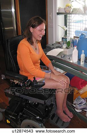 Stock Image - Young woman (wheelchair user) laughs as she prepares to repot a plant.. Fotosearch
