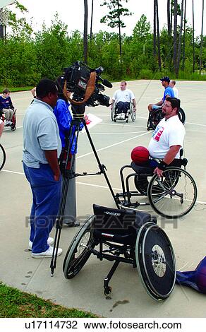 Stock Image - A group of men playing a game of wheelchair basketball at their local recreation center, being interviewed by the local news station.. Fotosearch