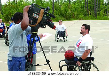 A group of men playing a game of wheelchair basketball at their local recreation center, with one who is being interviewed by the local news station. View Large Photo Image Stock Photo - A group of men playing a game of wheelchair basketball at their local recreation center, with one who is being interviewed by the local news station.. Fotosearch