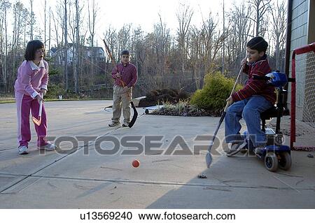 Stock Image - Boy on electric scooter and girl with Down syndrome playing street hockey with other children.. Fotosearch