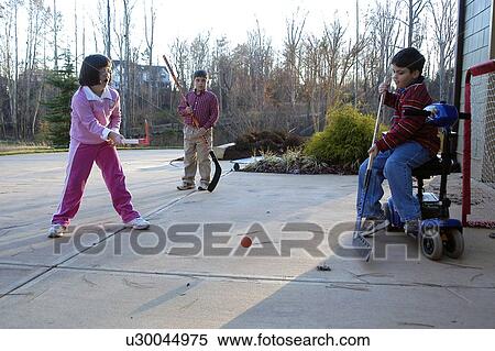 Stock Photography - Boy on electric scooter and girl with Down syndrome playing street hockey with other children.. Fotosearch