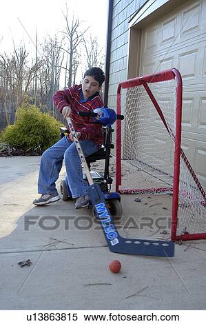 Stock Photography - Boy with disabilities practicing tending goal and playing hockey while sitting on his electric scooter.. Fotosearch