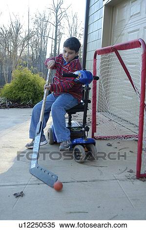 Stock Photography - Boy with physical disabilities guarding a hockey goal while sitting on his scooter.. Fotosearch