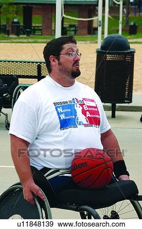 Stock Photo - Man with a disability (amputee), utilizing a wheelchair for mobility, preparing to play a game of basketball with his buddies at the local recreation center.. Fotosearch