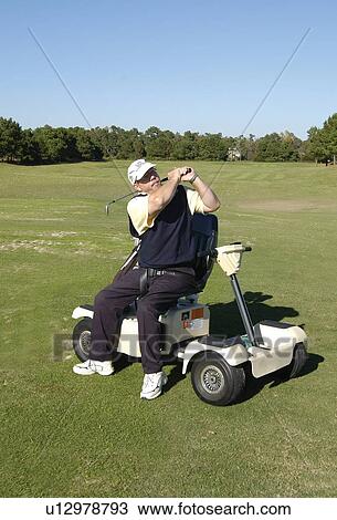Stock Image - Man with a disability playing golf at a golf course while sitting on his scooter that he uses for mobility.. Fotosearch