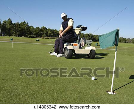 Stock Image - Man with a disability playing golf at a golf course while sitting on his scooter that he uses for mobility.. Fotosearch