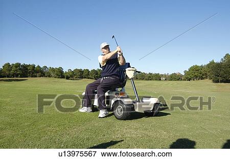 Stock Photo - Man with a disability playing golf at a golf course while sitting on his scooter that he uses for mobility.. Fotosearch