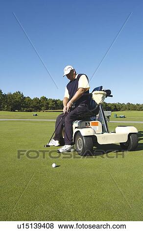 Stock Photo - Man with a disability playing golf at a golf course while sitting on his scooter that he uses for mobility.. Fotosearch