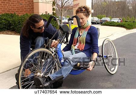 Man with a disability showing a person without a disability how to use his hand-controlled bicycle. View Large Photo Image Picture - Man with a disability showing a person without a disability how to use his hand-controlled bicycle.. Fotosearch