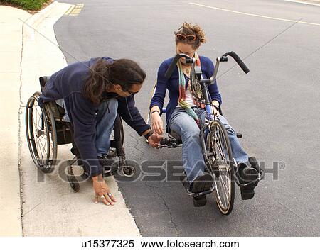 Man with a disability utilizing a wheelchair for mobility showing a friend how to ride a hand-controlled bicycle. View Large Photo Image Stock Photography - Man with a disability utilizing a wheelchair for mobility showing a friend how to ride a hand-controlled bicycle.. Fotosearch