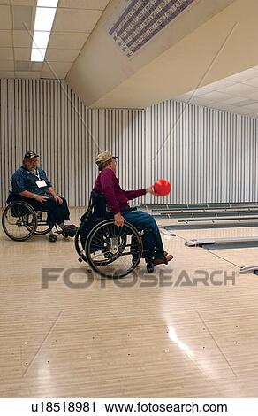 Stock Image - People with disabilities, utilizing wheelchairs for mobility, enjoying an evening bowling at their local bowling alley.. Fotosearch