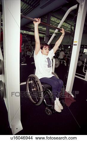 Woman with a disability, utilizing a wheelchair for mobility, working out in the weight room at her local fitness center. View Large Photo Image Picture - Woman with a disability, utilizing a wheelchair for mobility, working out in the weight room at her local fitness center.. Fotosearch