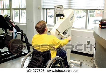 Stock Image - Young man with a disability, utilizing a wheelchair for mobility, working out at a local fitness center.. Fotosearch