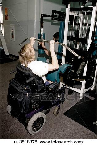 Stock Photo - Young woman with a disability, utilizing a wheelchair for mobility, working out on an exercise machine at her local fitness center.. Fotosearch
