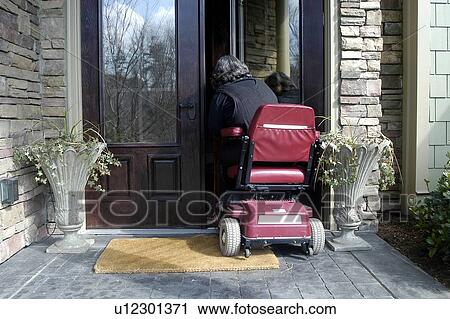 Stock Image - A woman using a wheelchair enters her home.. Fotosearch