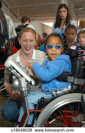 Stock Photo - Adorable little girl with a disability having a blast with friends and caregivers.. Fotosearch