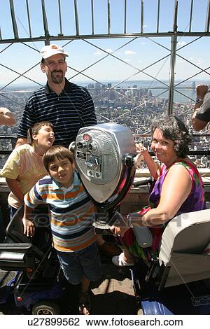 Stock Image - Happy family visiting New York City. Mom and one son have disabilities requiring scooters for mobility assistance.. Fotosearch