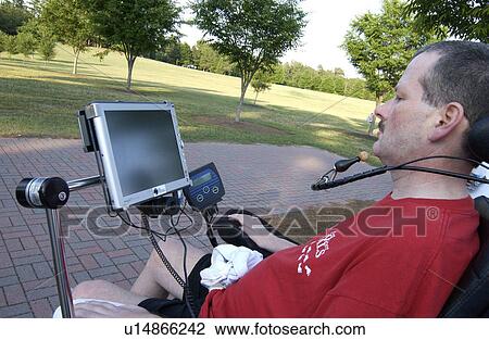Stock Image - Man with a disability utilizing a mouthpiece to give commands to communications system that allows him to communicate.. Fotosearch