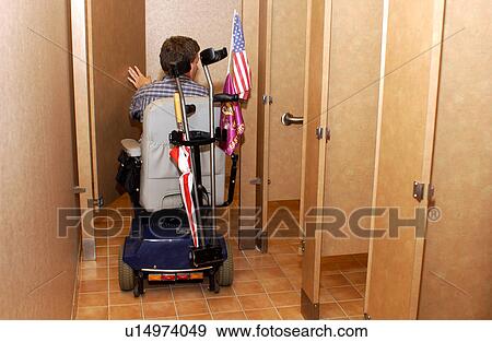 Stock Photo - Man with disability, utilizing a scooter for mobility, entering a tight handicap or accessible stall to use the restroom.. Fotosearch