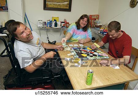 Stock Photograph - Three friends playing a board game and having a good time. The two men have disabilities, and live in the apartment together.. Fotosearch