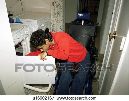 Woman with a disability, utilizing a wheelchair for mobility, doing her laundry in her apartment. View Large Photo Image Stock Photo - Woman with a disability, utilizing a wheelchair for mobility, doing her laundry in her apartment.. Fotosearch