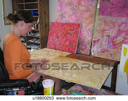 Stock Image - Young woman (wheelchair user) applies texture to her artwork.. Fotosearch