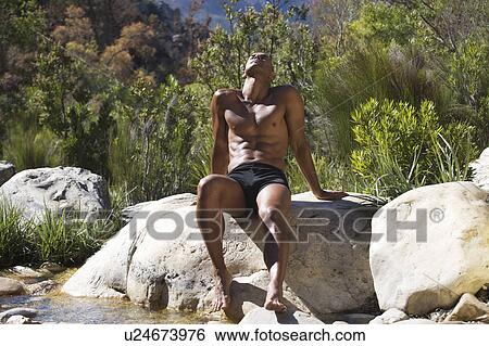 Stock Photograph - Young athletic man sitting in a natural setting. Fotosearch