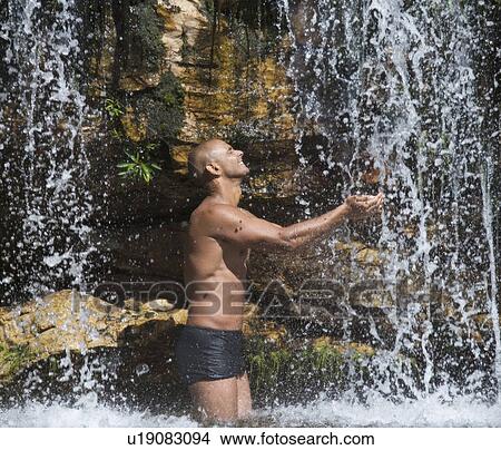 Picture - Young man standing in a waterfall. Fotosearch