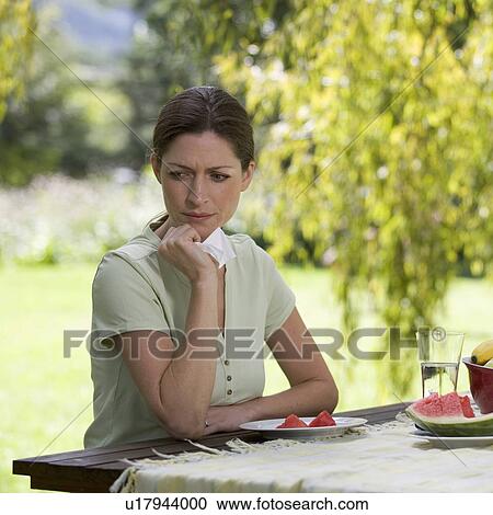 Stock Image - A woman looking sad and pensive sitting in the garden. Fotosearch