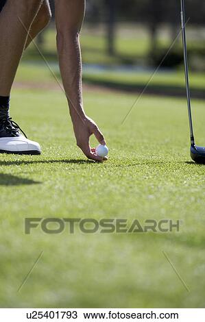 Stock Image - Man playing golf, close-up of feet on the tee. Fotosearch