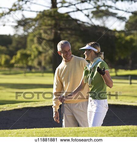 Stock Image - Man teaching a woman how to play golf. Fotosearch