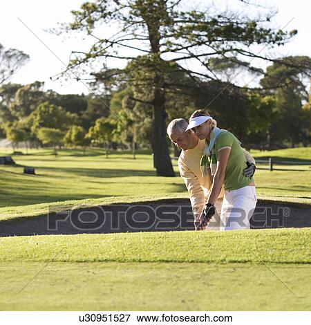 Stock Photo - Man teaching a woman how to play golf. Fotosearch