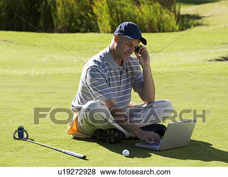Stock Photo - Man using a laptop and mobile phone whilst on the golf course. Fotosearch