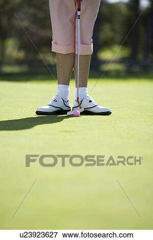 Stock Photo - Woman playing golf, close-up of feet and putter. Fotosearch