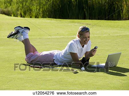 Woman using a laptop and mobile phone whilst on the golf course View Large Photo Image Stock Photograph - Woman using a laptop and mobile phone whilst on the golf course. Fotosearch