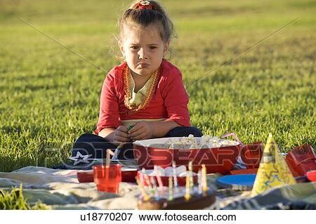 Stock Photo - A unhappy young girl having a birthday picnic. Fotosearch