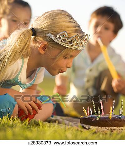 Stock Image - A young girl blowing out the candles on her birthday cake. Fotosearch