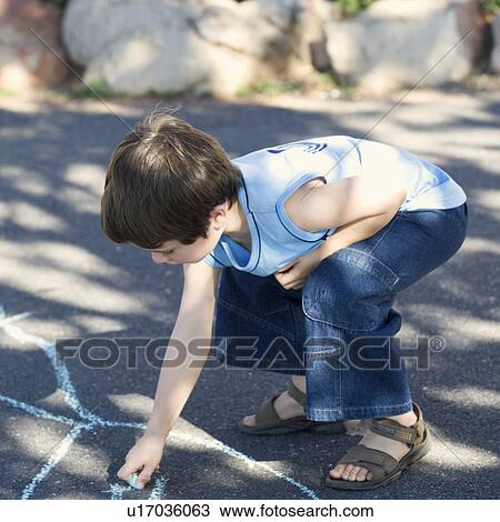 Stock Image - Young boy writing in chalk on the playground. Fotosearch