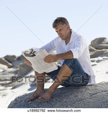 A man sitting on rocks reading a newspaper View Large Photo Image Stock Image - A man sitting on rocks reading a newspaper. Fotosearch
