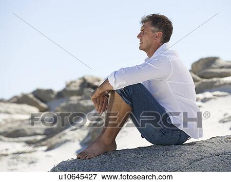 Stock Photo - A man sitting on rocks. Fotosearch