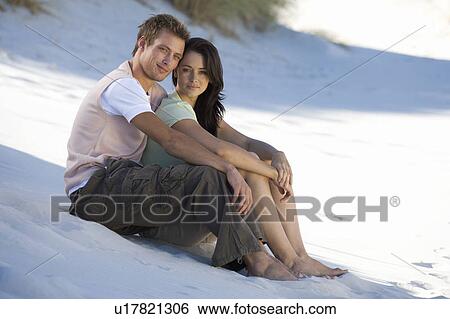 Stock Photograph - A young couple sitting on a beach. Fotosearch