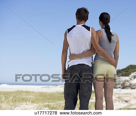 Stock Photo - A young couple standing on a beach. Fotosearch