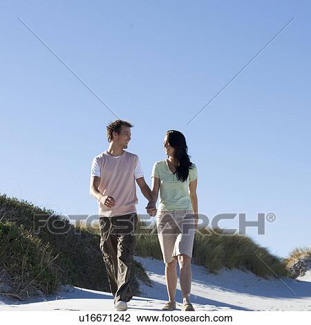 Stock Image - A young couple walking in sand dunes. Fotosearch